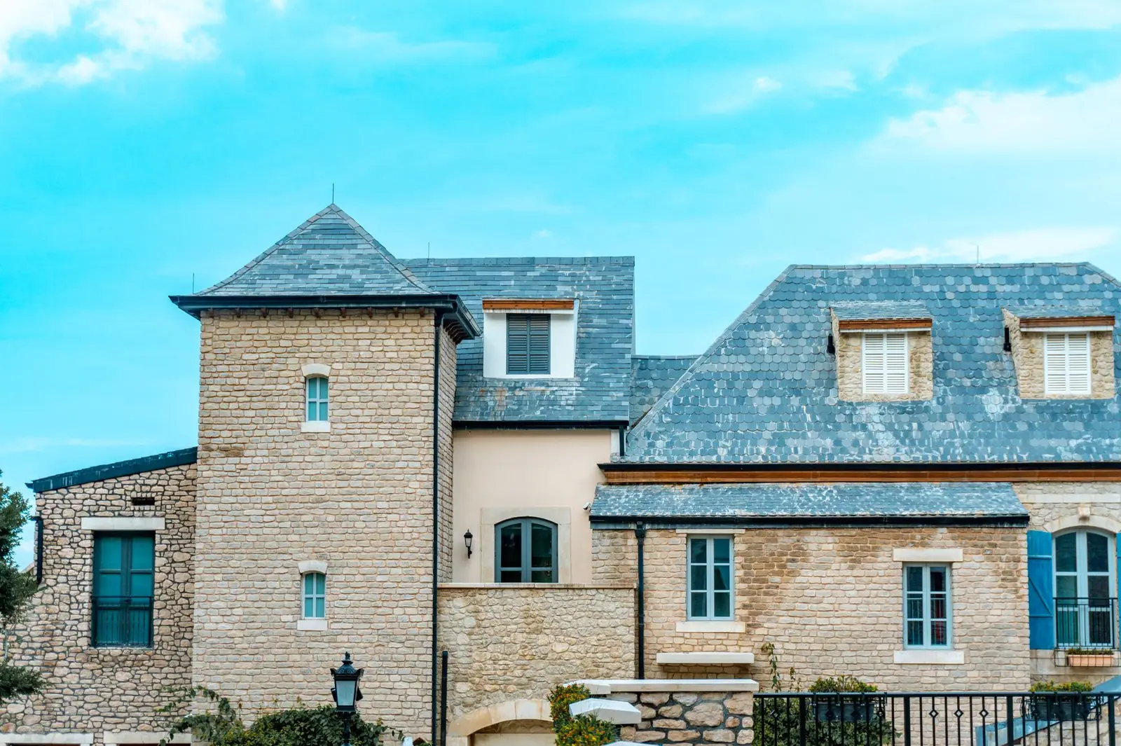 Toiture en ardoises bleutées sur un bâtiment en pierre claire, lucarnes et volets bleus