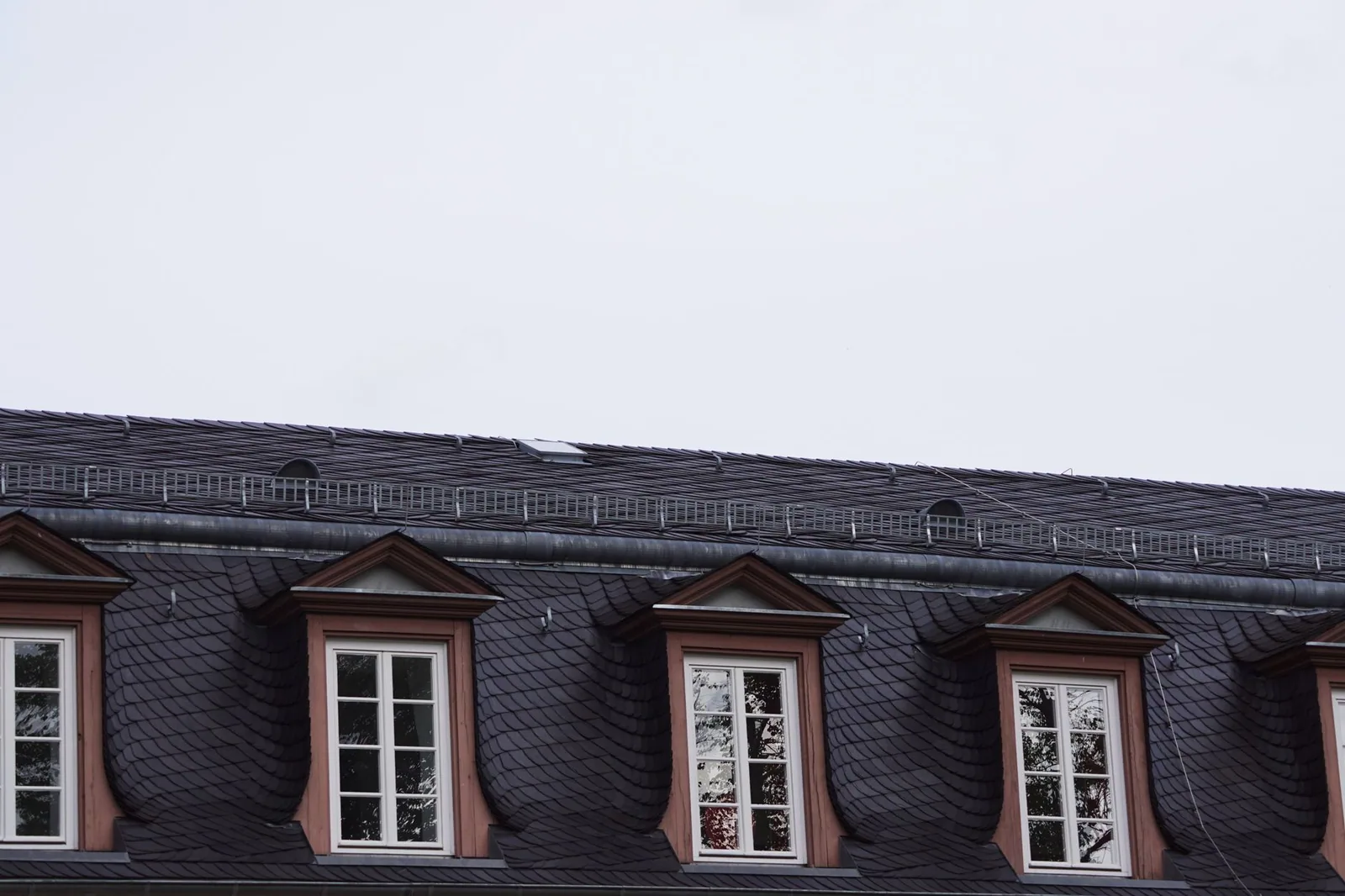 Immeuble couvert d'ardoises, lucarnes alignées et souches de cheminée sur le versant