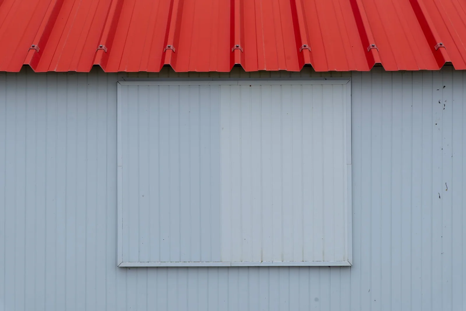 Rive d'une toiture métallique rouge sur un mur clair