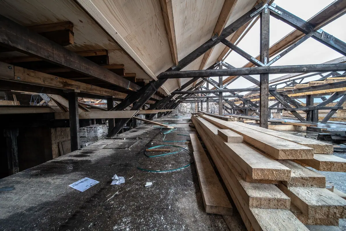 Comble non aménagé, fermes de charpente apparentes et planches entreposées au sol