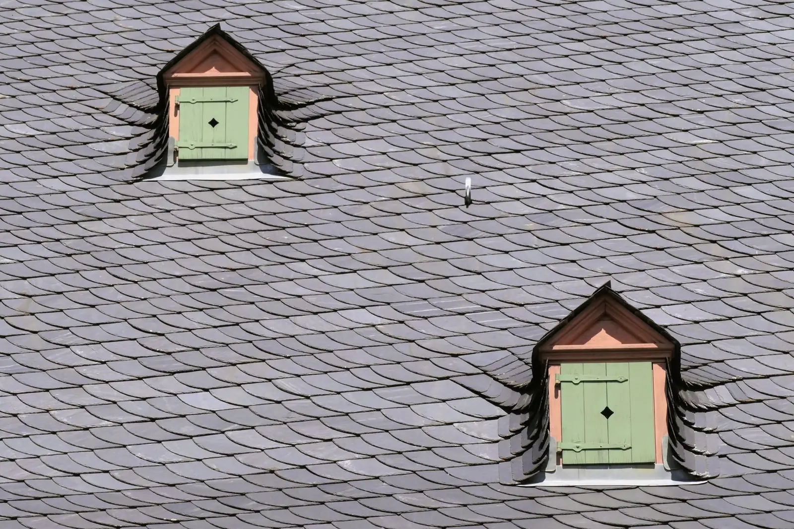 Deux petites lucarnes encastrées dans un versant d'ardoises, avec leur raccord de couverture visible tout autour