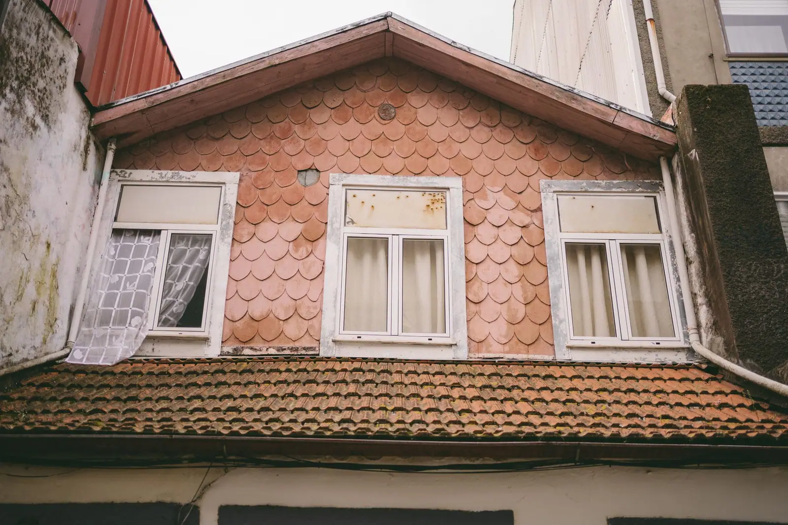 Pignon d'une maison ancienne couvert de petites tuiles en écaille, fenêtres alignées sous la rive