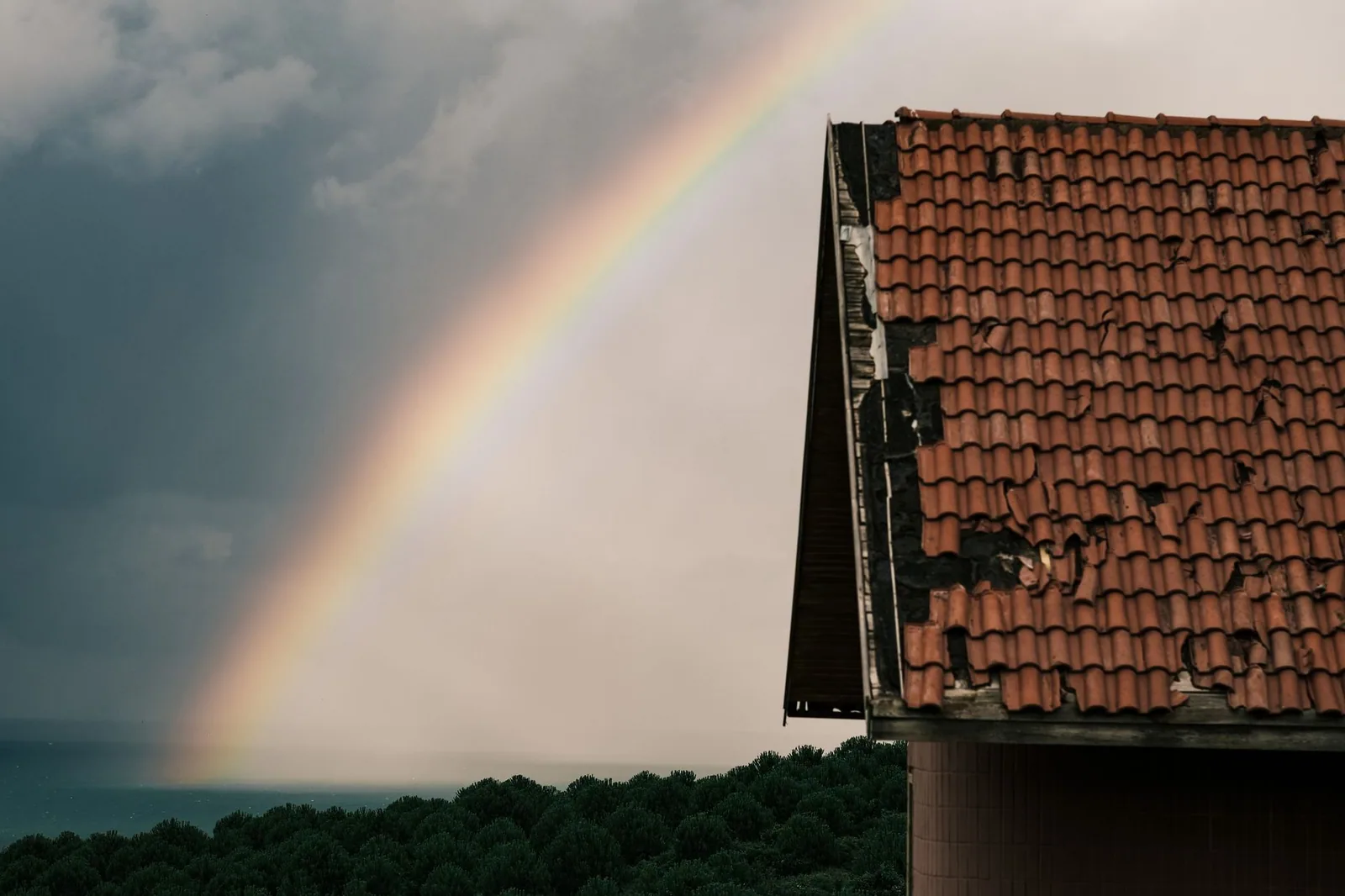 Toiture se détachant sur un ciel d'orage traversé d'un arc-en-ciel