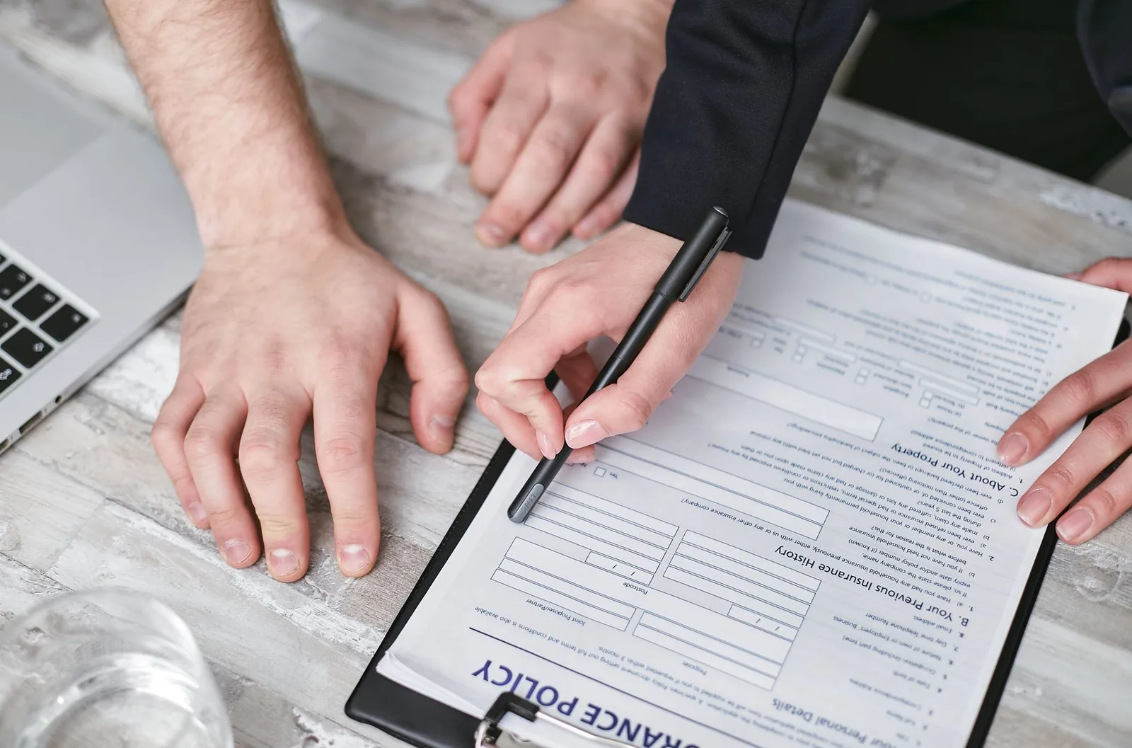 Mains remplissant un formulaire de police d'assurance posé sur un bureau, stylo à la main
