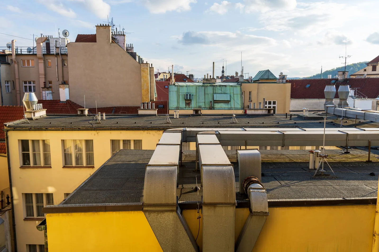 Toits plats d'immeubles urbains couverts d'un revêtement bitumineux, bordés d'acrotères et traversés par des gaines de ventilation et des conduits