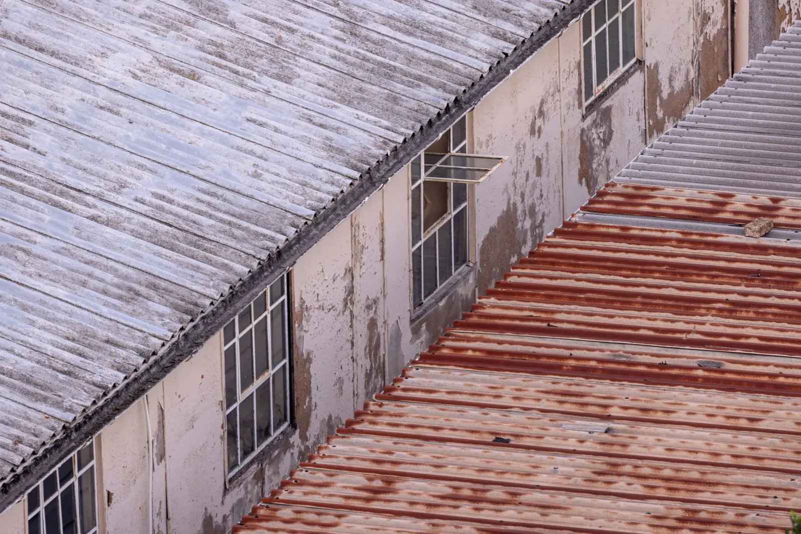 Toiture ondulée en plaques de fibrociment sur un bâtiment ancien, patinée et couverte de mousse