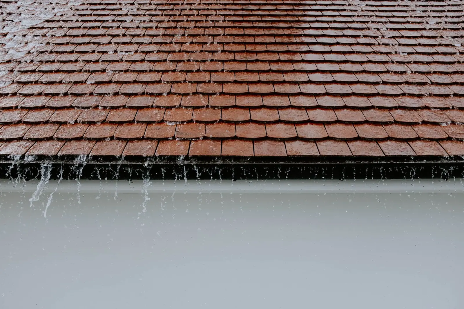 Pluie battante sur une couverture en tuiles plates, l'eau ruisselle en nappe au bord du versant