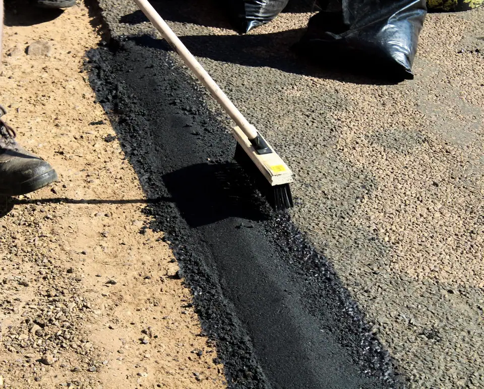 Produit noir étalé à la raclette sur une surface plane gravillonnée