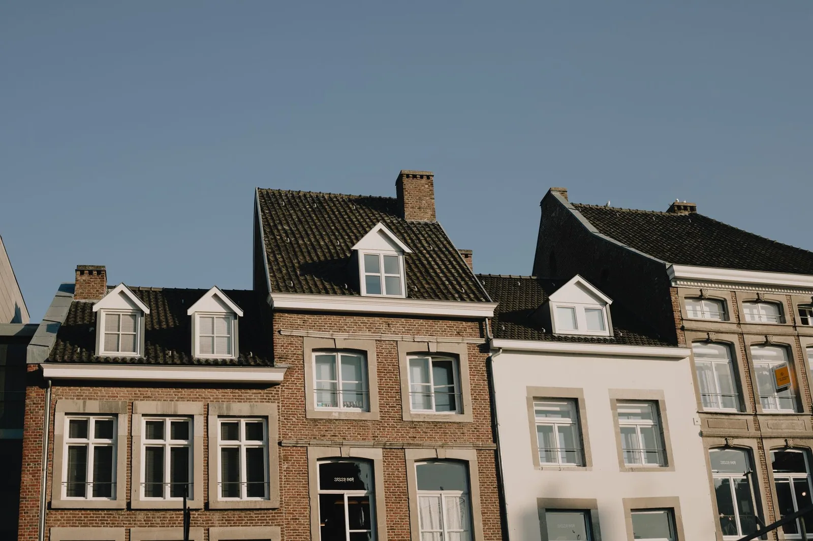 Rangée d'immeubles européens aux toitures sombres et aux lucarnes alignées, vus depuis la rue