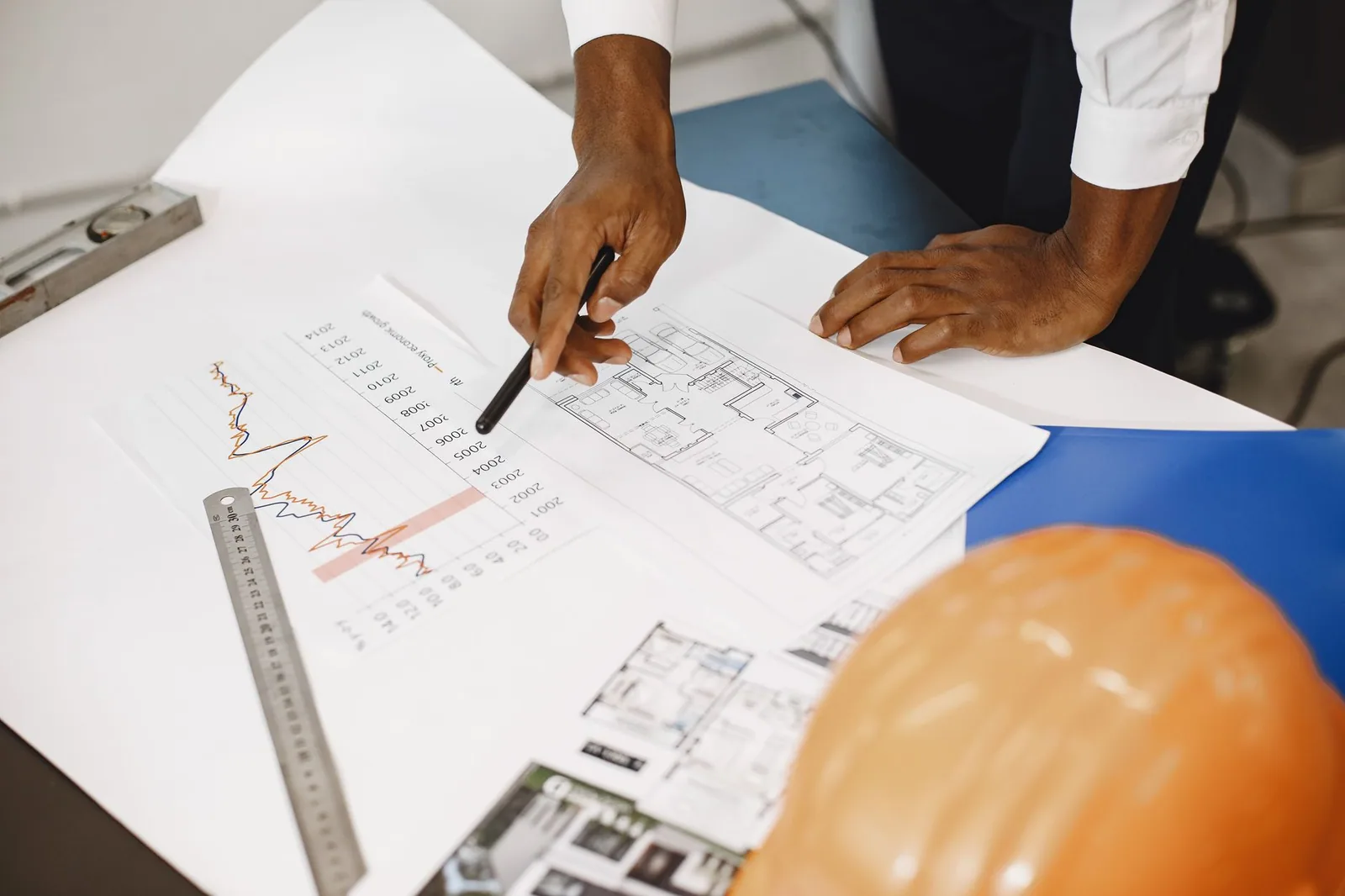 Mains annotant un plan d'architecte sur une table, casque de chantier posé à côté