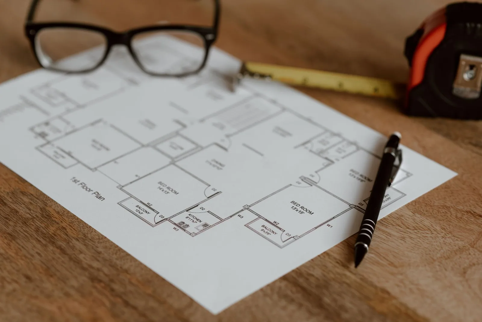 Plan de maison posé sur une table, stylo, lunettes et mètre à ruban à côté