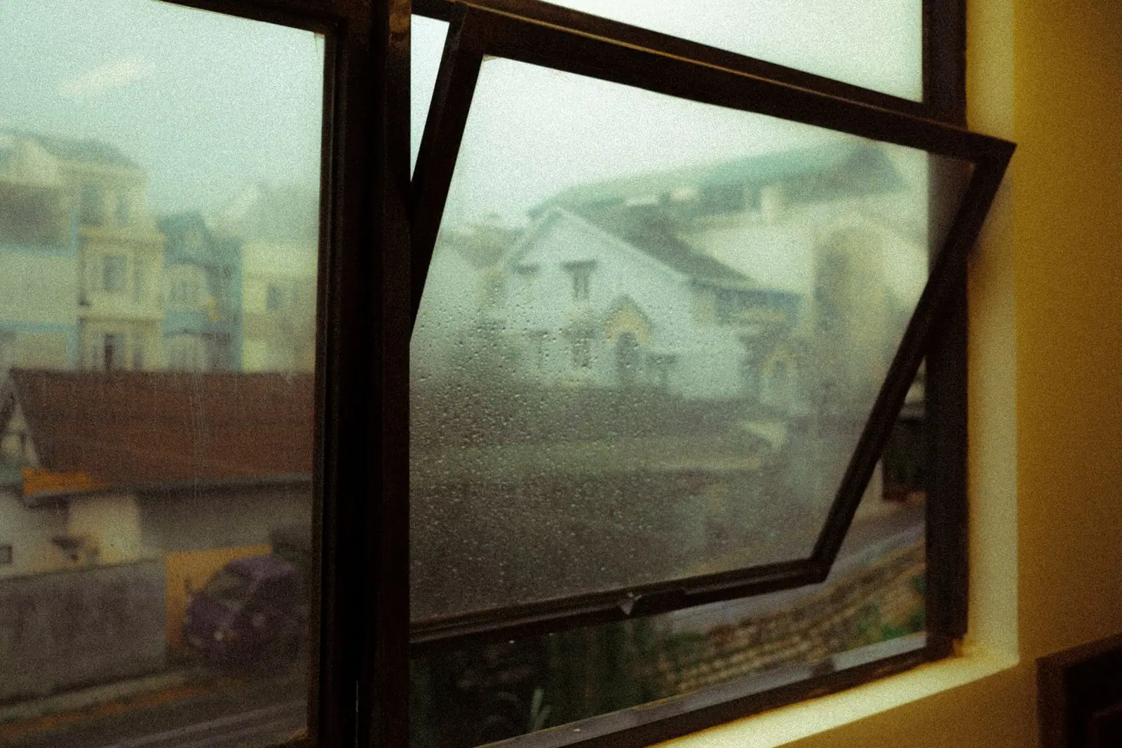 Fenêtre ouverte sur un paysage de toits sous la pluie