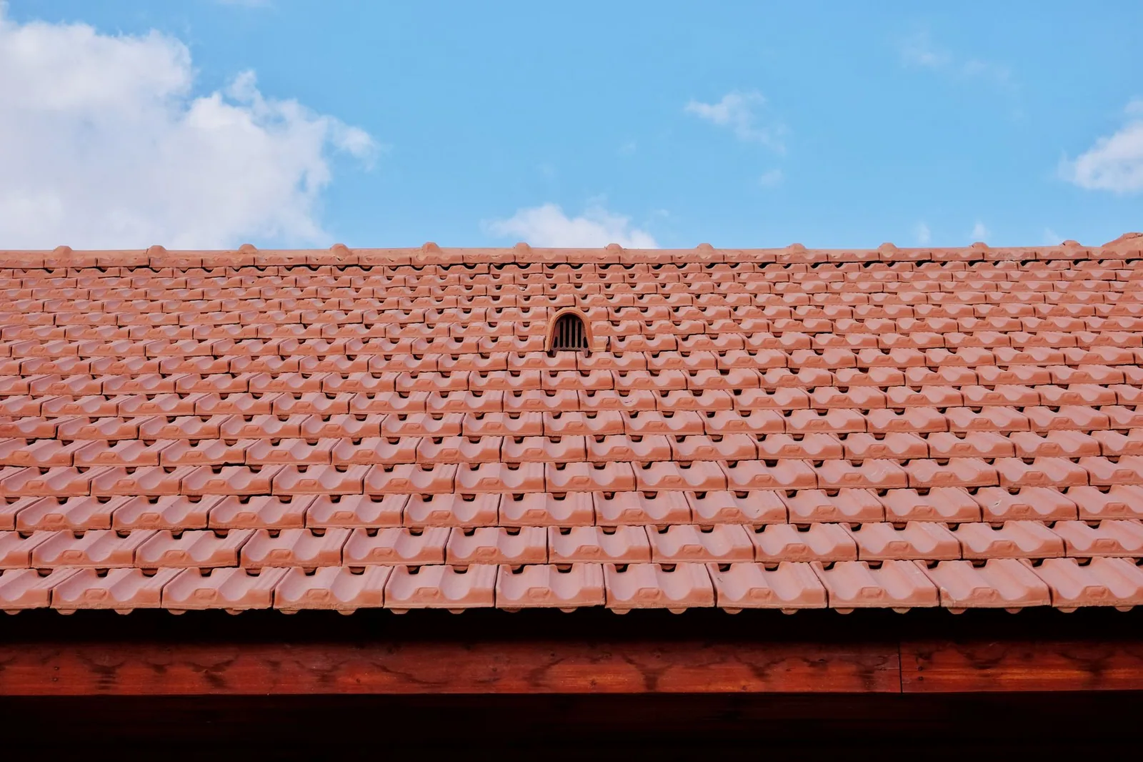 Versant de tuiles rouges percé d'une tuile de ventilation, vu depuis le sol